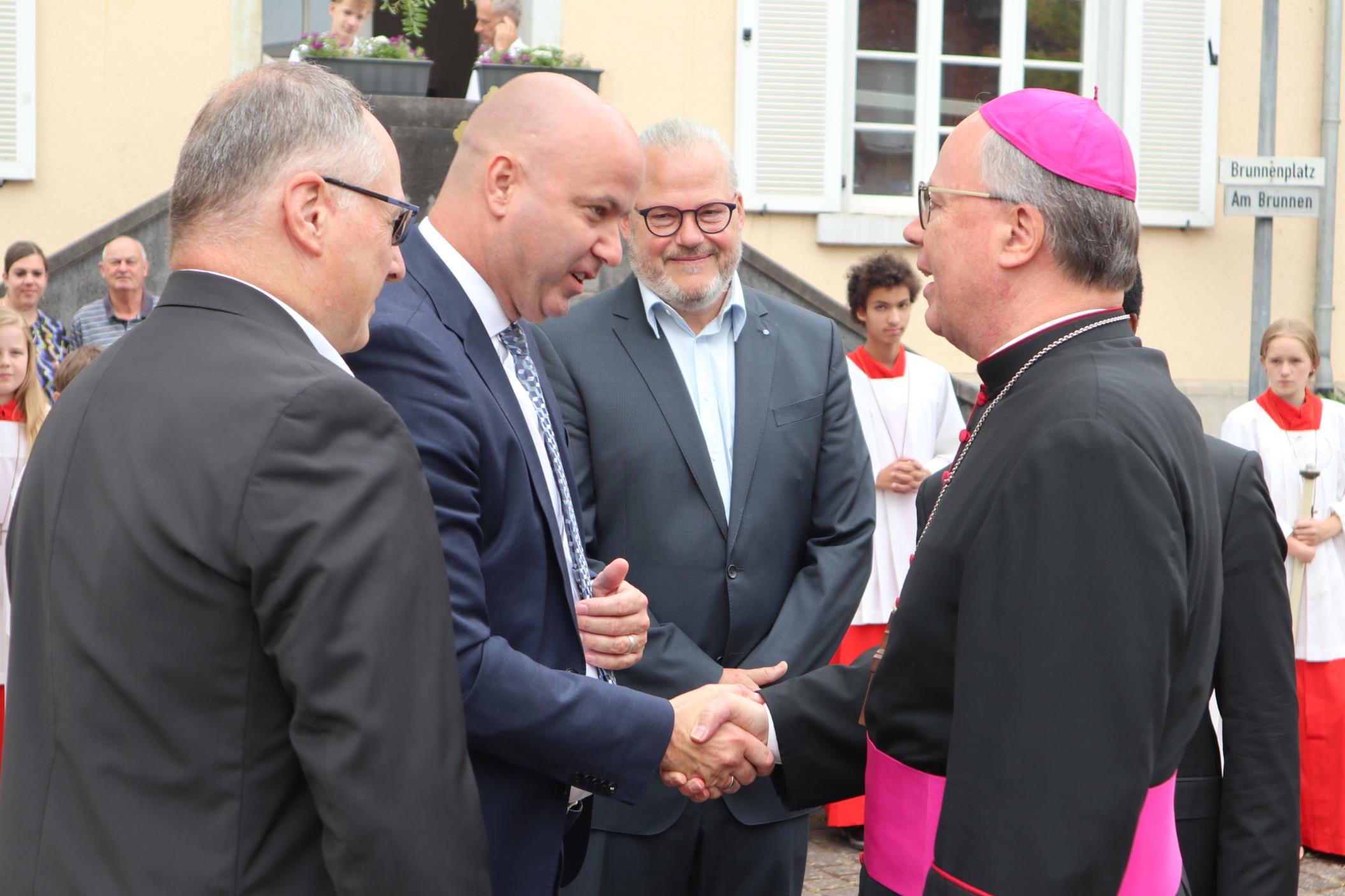 Bischof Ackermann wird von Ortsbürgermeister Peter Schermuly (links), Verbandsbürgermeister Michael Cyfka (Zweiter v. links) und Stephan Klöckner, Vorsitzender Verwaltungsrat, begrüßt.